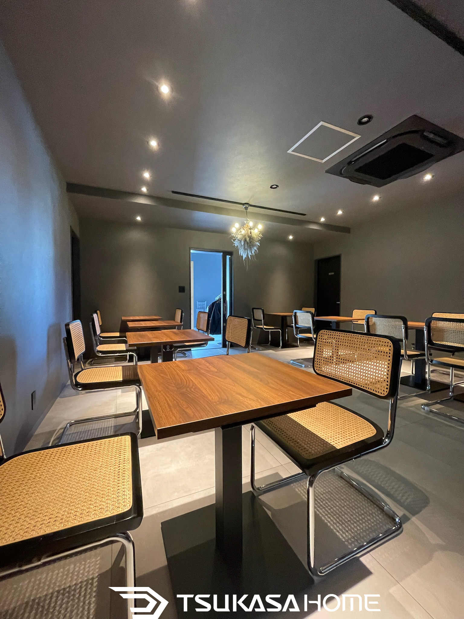 マットグレーの内装に木製テーブルとスチールチェアを配した落ち着いた店舗空間。ツカサホーム施工。