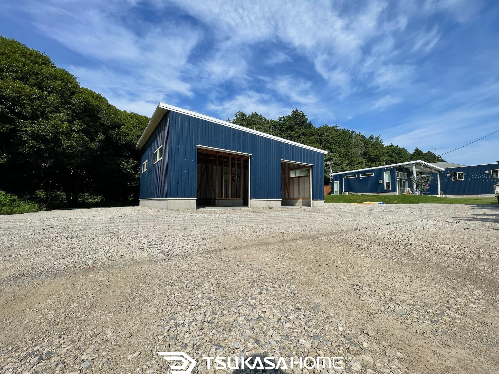 青いガルバリウム外壁の木造倉庫。シャッター開口部が見える建築中の外観。ツカサホーム施工。