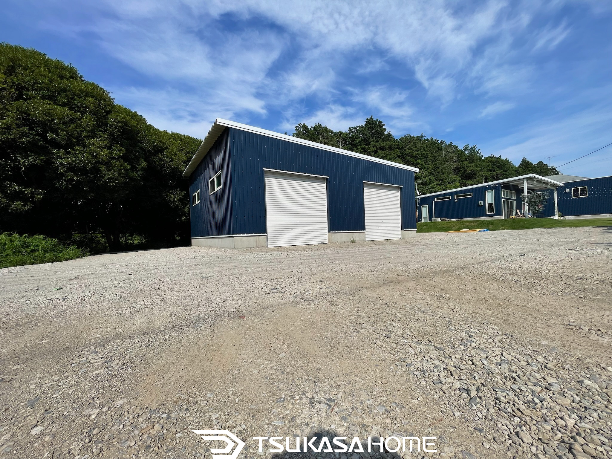 青いガルバリウム外壁の木造倉庫外観。2台分のシャッターを備えたシンプルなデザイン。ツカサホーム施工。